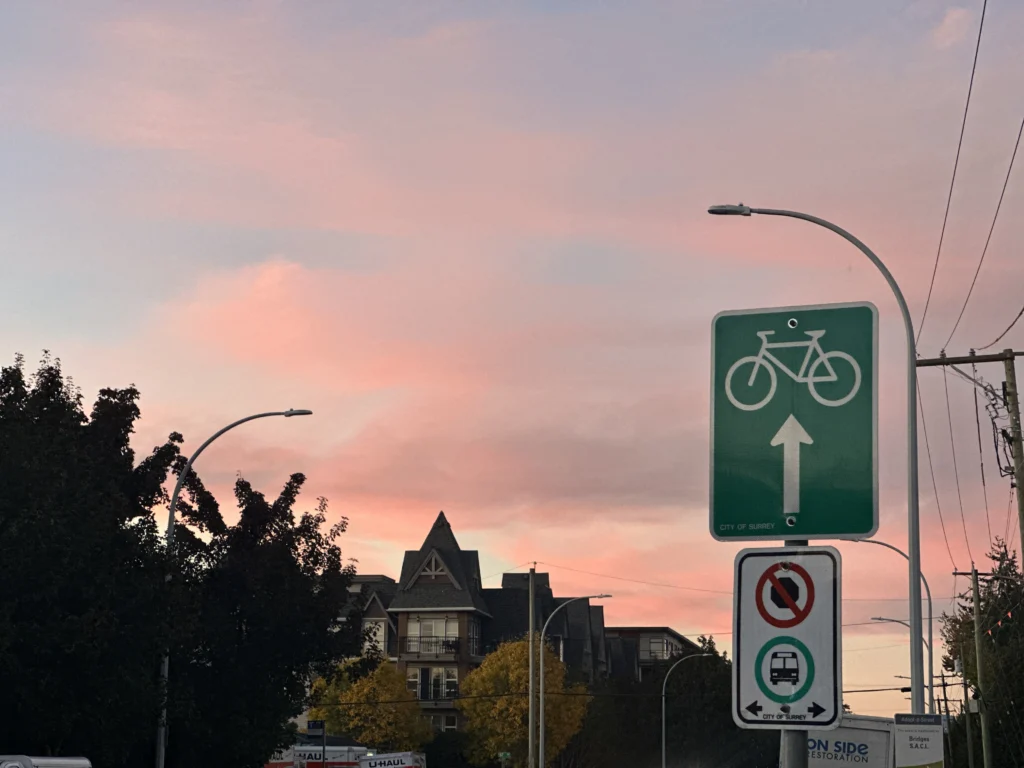 City of Surrey street at sunset with pink skies and bicycle lane sign, symbolizing urban community life and sustainable city culture in Canada.